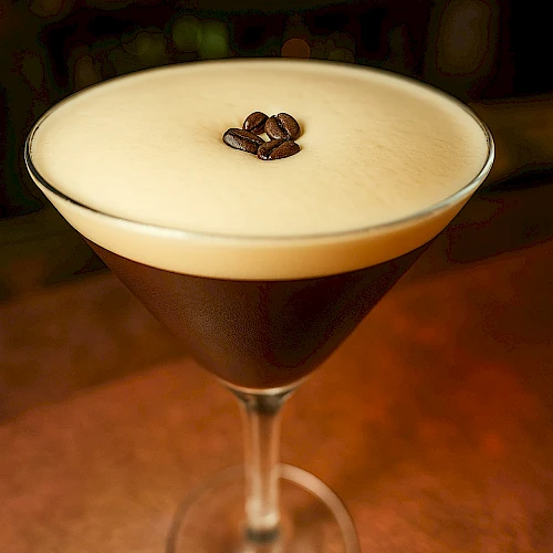 A martini glass with a dark coffee-like cocktail and a frothy cream layer, topped with a single coffee bean.