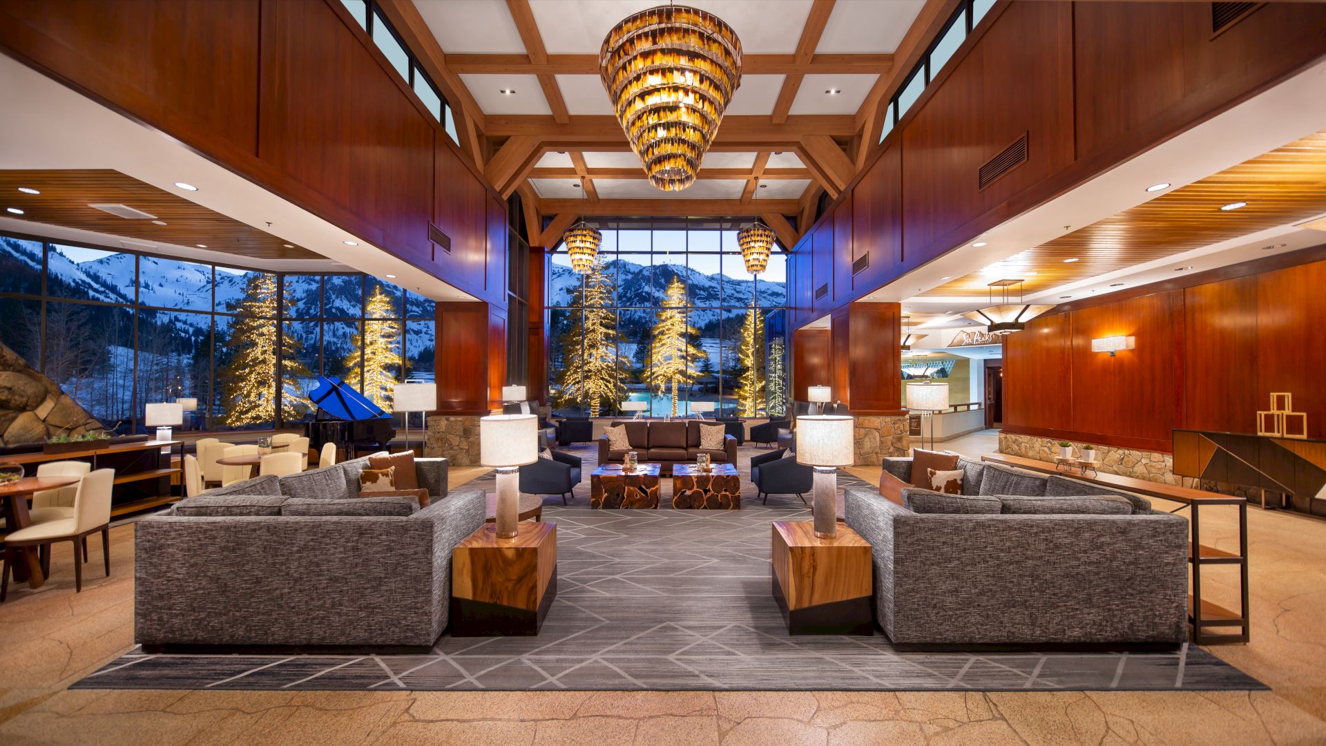 A modern and spacious lobby with large windows showcasing a snowy landscape. Features cozy seating, wooden accents, and elegant chandeliers.