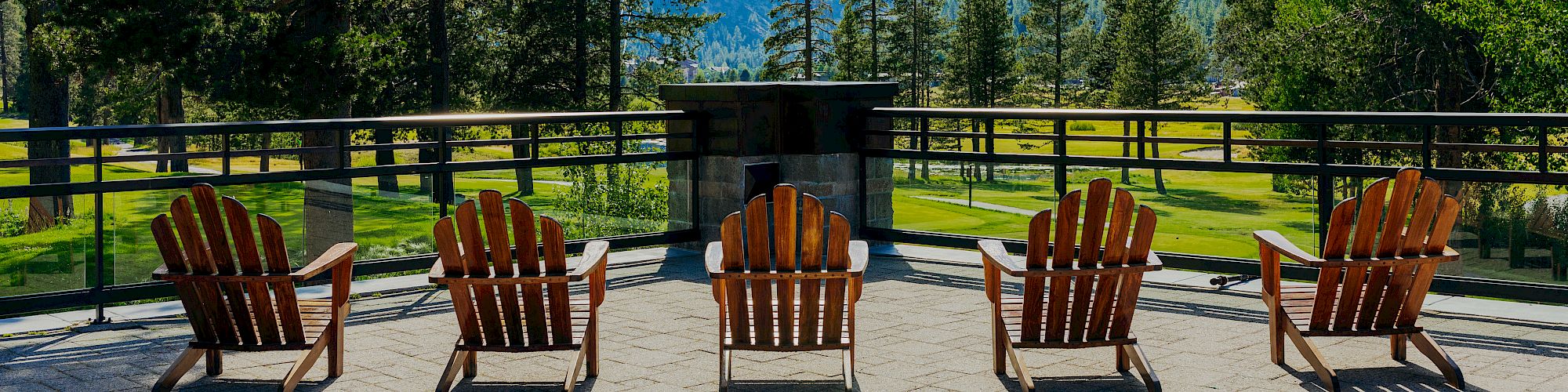 Four wooden chairs placed on a stone patio facing a scenic view of trees, mountains, and a clear sky with a small cloud.