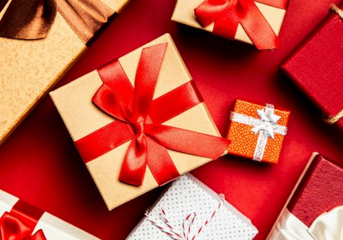 A festive assortment of wrapped gift boxes with ribbons and bows on a red background, perfect for celebrations.