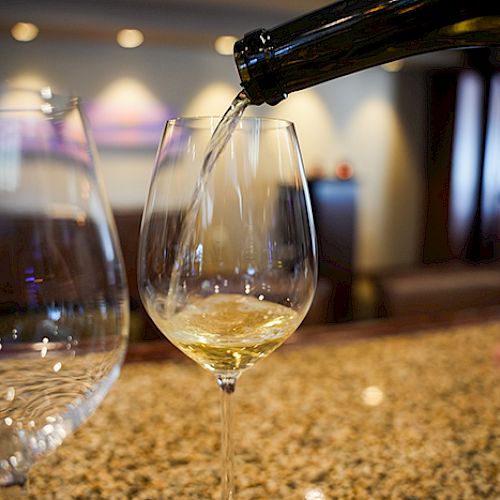 Pouring white wine into a stemmed glass at a bar, with another empty glass nearby.