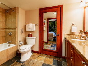 A modern bathroom with a large tiled shower/bath, wooden-framed mirror, double sink vanity, and a cozy, warm-toned palette.