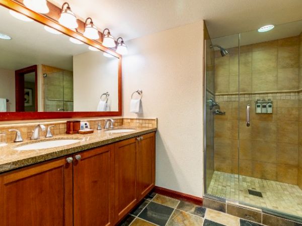 The image shows a modern bathroom with a double sink vanity and a glass-enclosed shower on a tiled floor.