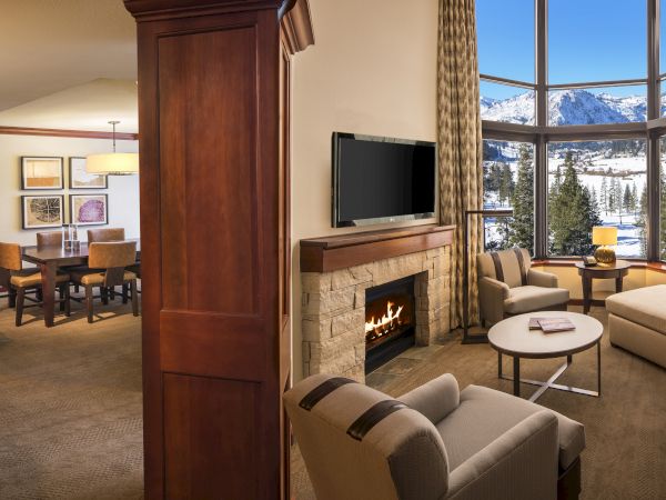A cozy living area with a fireplace, mountain view, kitchen, and dining area, featuring warm lighting and contemporary decor finishing.