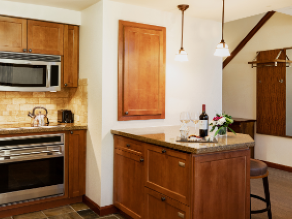 A kitchen with wooden cabinets, a microwave, oven, and island. Wine, glasses, and flowers are on the counter. Cozy and inviting atmosphere.