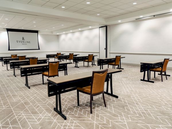 A conference room with spaced-out tables and chairs facing a projector screen displaying the Everline logo.