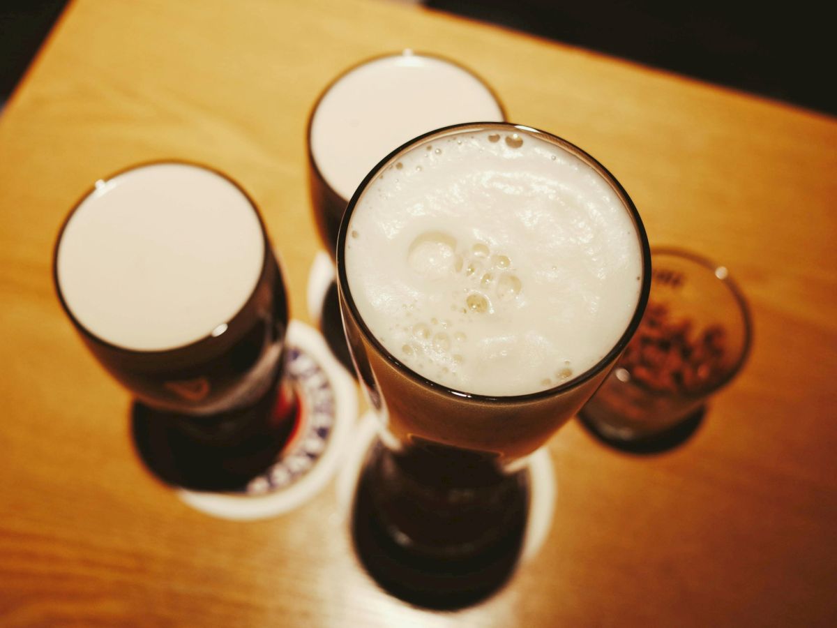 Assorted beer glasses on a wooden table, frothy tops, viewed from above, with coasters and a warm, dim setting.