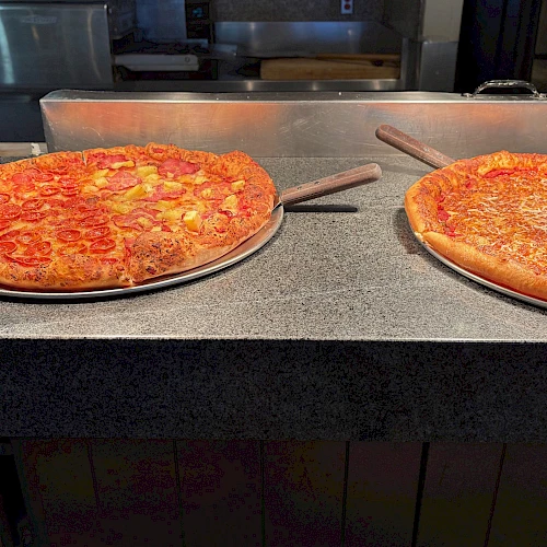 Two pizzas on a counter, cheese and pepperoni, fresh out of the oven and ready to slice.