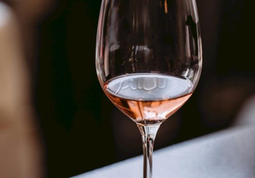 A wine glass with a small amount of pink ros&eacute; sits on a bar counter, blurred background, soft lighting, and the stem and base visible.
