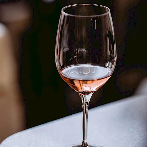 A wine glass with a small amount of pink ros&eacute; sits on a bar counter, blurred background, soft lighting, and the stem and base visible.