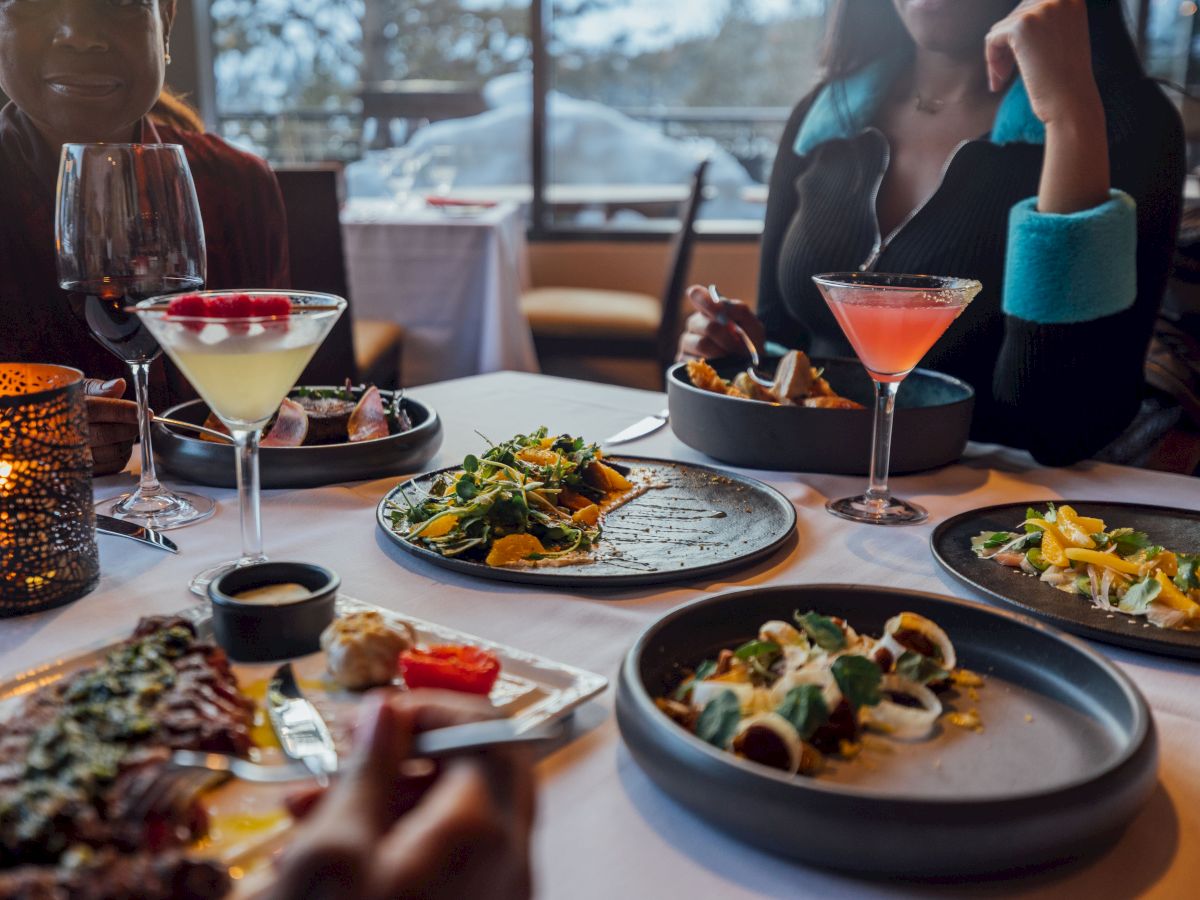 People dining at a restaurant, enjoying cocktails and a variety of dishes at a beautifully set table.