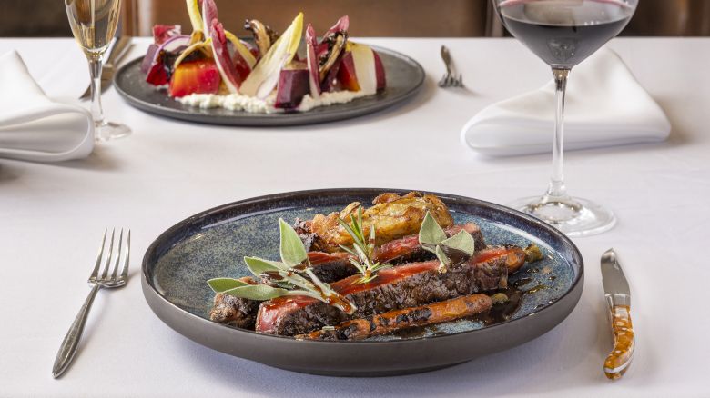 A table set with a dish of roasted vegetables in the foreground, a salad in the background, a glass of red wine, and napkins.