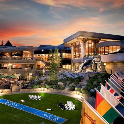 A warmly lit resort building at sunset with patios, landscaping, and a stone fountain in the foreground.