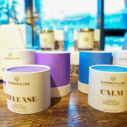 The image shows candle jars with labels "RELEASE" and "CALM," branded "ILLUMINATE LIFE," placed on a wooden table with more candles in the background.