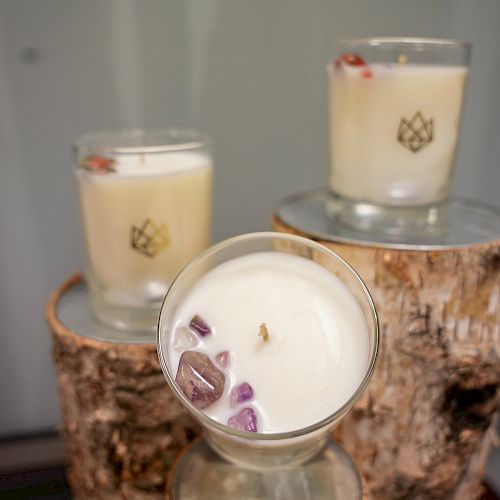 Three lit candles in glass holders with crystal decorations are displayed on wooden logs.