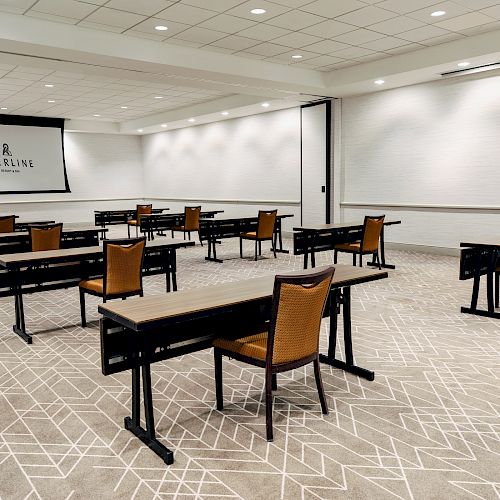 An empty conference room is set up with individual desks and chairs facing a projection screen with the word 