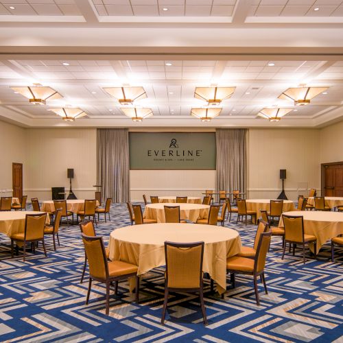A banquet-style meeting room with round tables, chairs, draped curtains, and an EVERESTINE logo banner under skylight lighting.