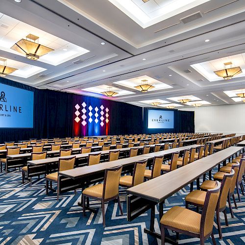 A conference room with rows of tables and chairs facing two screens on the far wall, with 