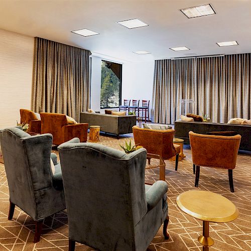 A well-lit room with several armchairs, a few tables, and large windows covered by curtains. The floor is carpeted in a geometric pattern.