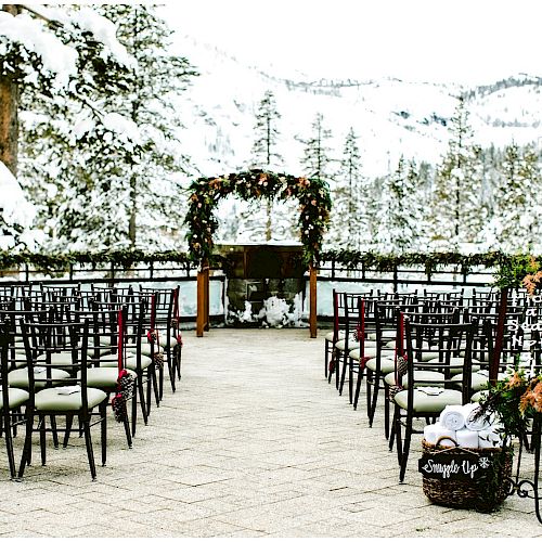 An outdoor wedding setup in a snowy mountain setting with decorated chairs and an archway adorned with greenery and flowers, ending the sentence.