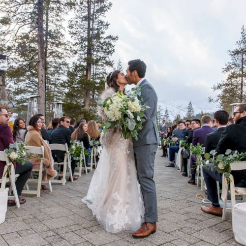Outdoor wedding&mdash;bride and groom kiss as guests line the aisle with bouquets in a forested mountain setting.
