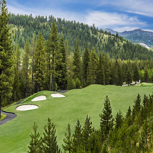 A scenic golf course nestled within a lush, forested mountain landscape with sand traps and a winding path among the tall trees.