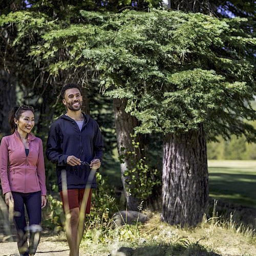 Two people walking along a forest path, smiling and enjoying the outdoor scenery.