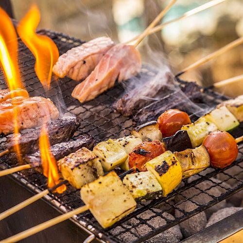 A barbecue grill with skewers of meat and vegetables cooking over an open flame. Smoke is rising from the food, which looks delicious.