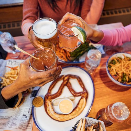 Friends dine at a caf&eacute; table with hot breakfast plates, sausages, eggs, fries and coffee, sharing drinks and snacks.