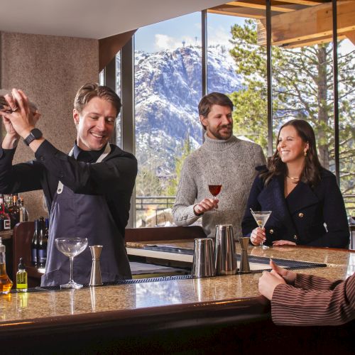 A bartender pours drinks for friends during a cozy tasting at a bar with a mountain view.
