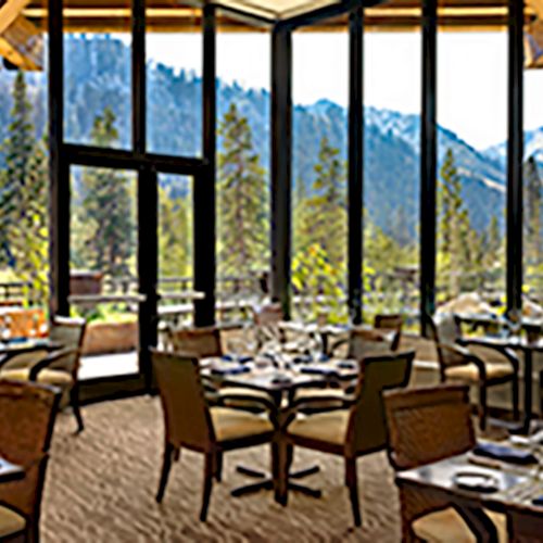 This image shows a restaurant with large windows, providing a scenic view of mountains and trees, with tables set for dining indoors.