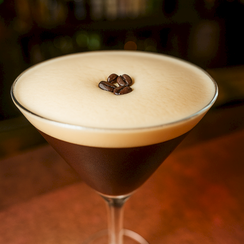 A creamy coffee cocktail in a martini glass, topped with three coffee beans against a softly blurred bar background.