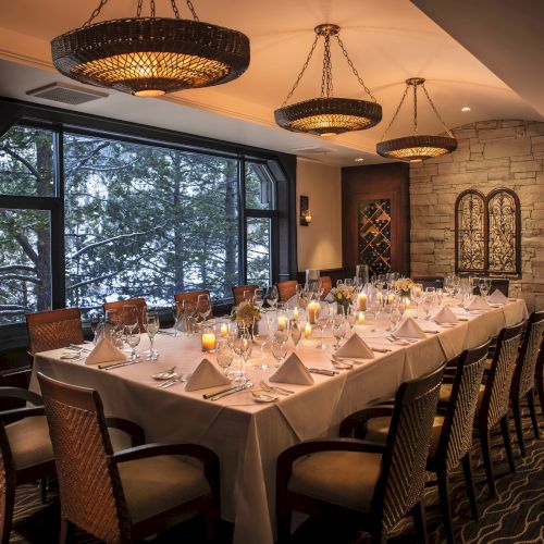 A well-decorated dining room with a long table set for a formal dinner, featuring elegant lighting, large windows, and neatly arranged place settings.