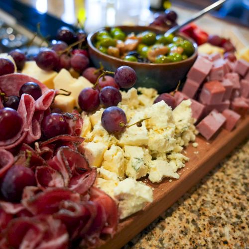 A charcuterie spread with grapes, prosciutto, cheese, and olives on a wooden board for a party platter.