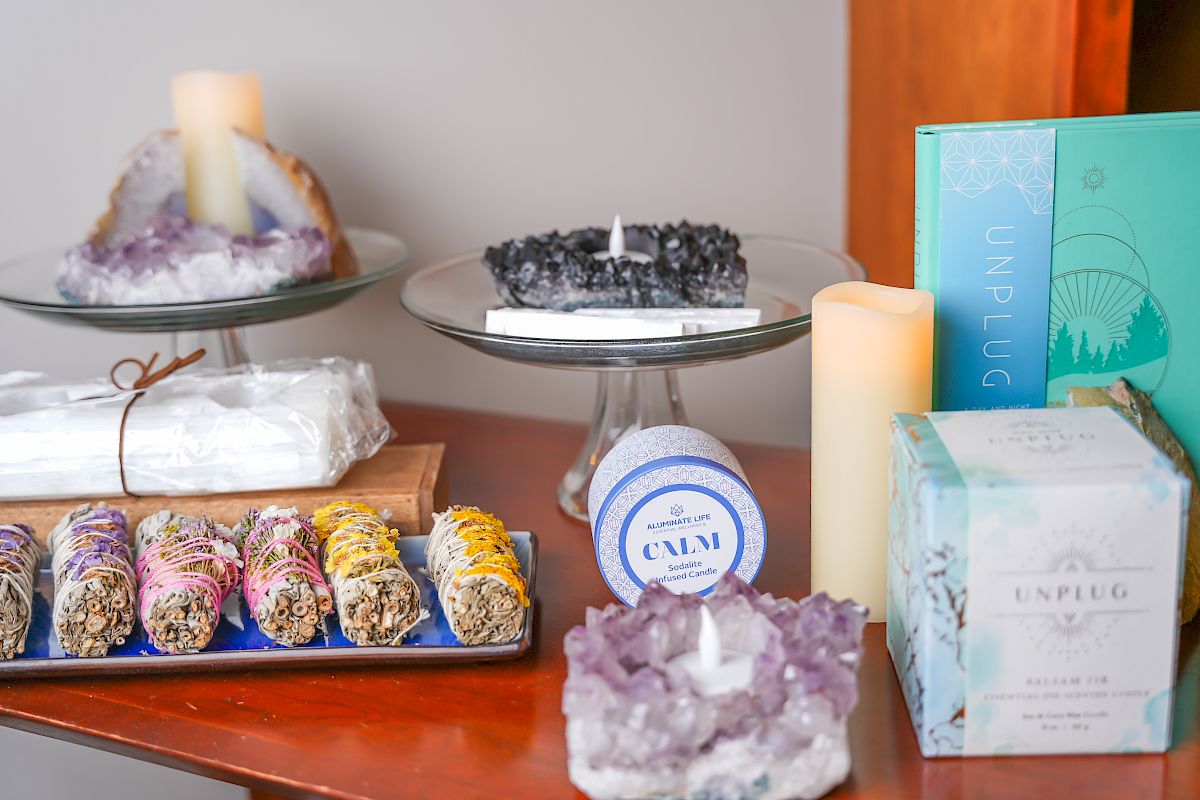 The image shows a display of crystals, candles, sage bundles, and boxed products arranged neatly on a wooden surface.