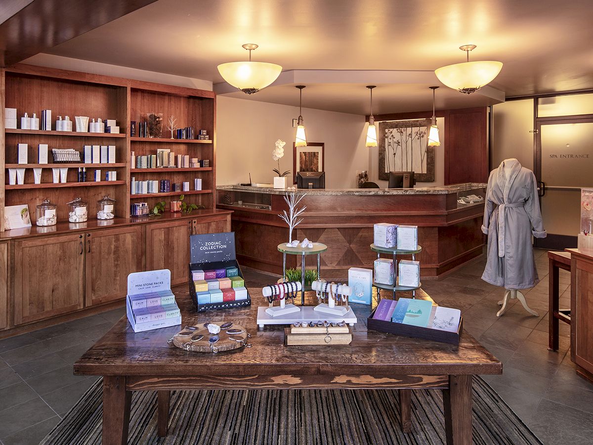 A well-organized spa or boutique store with wooden shelves, various products, a front counter, and a mannequin in a robe on display.