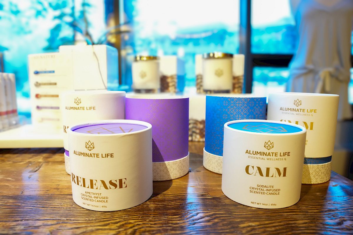 The image shows candles labeled "RELEASE" and "CALM" from the Aluminate Life brand, displayed on a wooden surface with more products in the background.