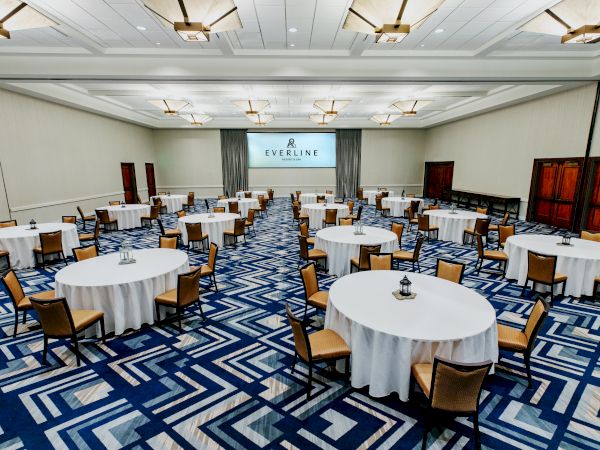 A conference room setup with round tables and chairs, white tablecloths, and a screen in front displaying "EVERLINE" in a bright, modern space.