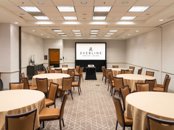 A bright conference room setup with round tables and a screen showing &ldquo;Everline Resort & Spa&rdquo; branding.