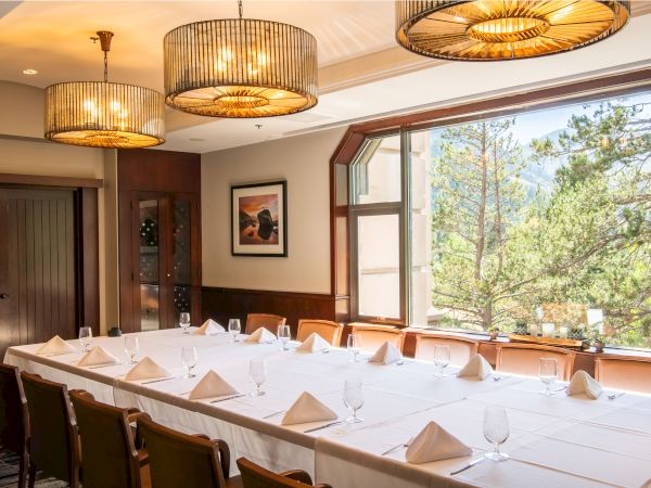 A cozy restaurant dining room with set tables, large windows, and glowing hanging chandeliers in a warm mountain setting.