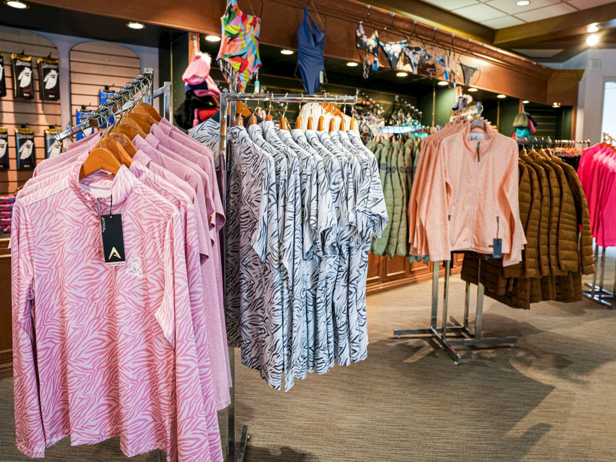 A clothing store displays shirts and jackets on racks, with a variety of colors and patterns, and accessories hung above.