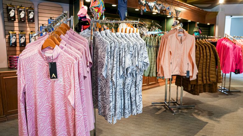 A clothing store displays shirts and jackets on racks, with a variety of colors and patterns, and accessories hung above.