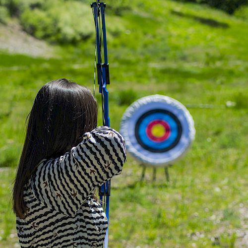 A person is aiming a bow and arrow at archery targets positioned on a grassy field.