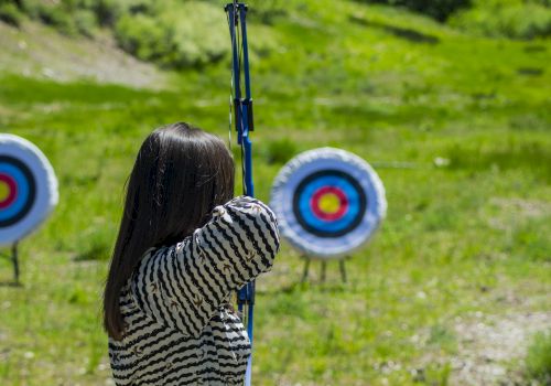 A person is practicing archery outdoors, aiming at two target boards set up in a grassy area.