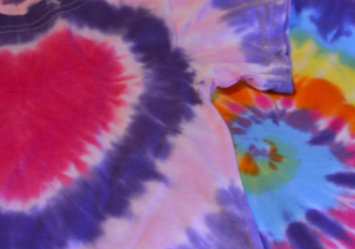 This image shows tie-dye shirts with vibrant, colorful patterns, including a red heart design on one shirt and various colorful swirls on another.