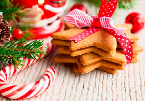 Star-shaped cookies tied with a ribbon are surrounded by candy canes, pine cones, and festive decorations on a wooden surface.