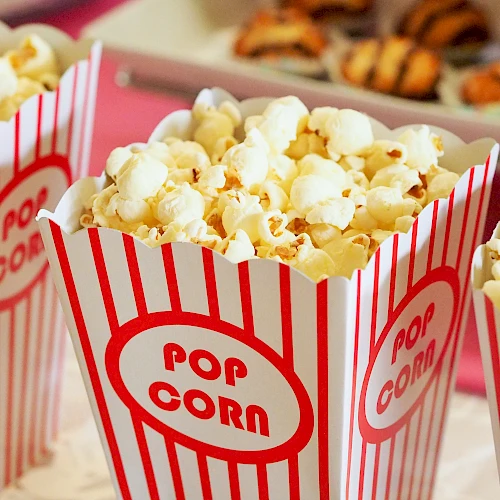 The image shows three containers filled with popcorn in red and white striped boxes labeled "Pop Corn" with some dessert items visible in the background.