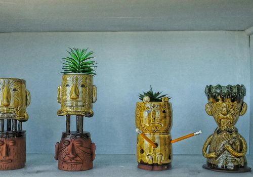 Colorful carved totems with quirky faces, some stacked, one with a plant sprouting, all quirky figurines on a shelf.