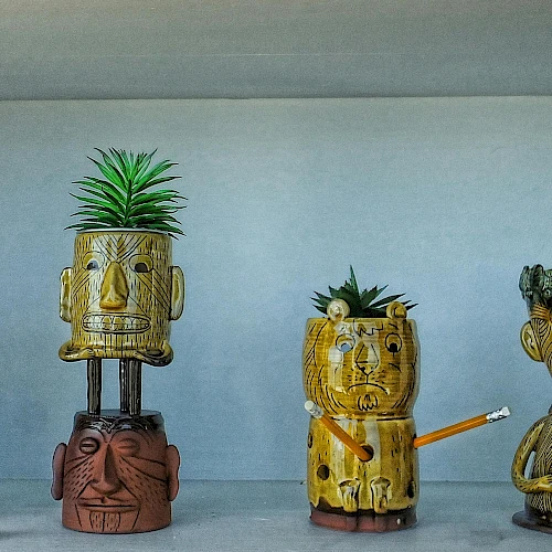 Colorful carved totems with quirky faces, some stacked, one with a plant sprouting, all quirky figurines on a shelf.