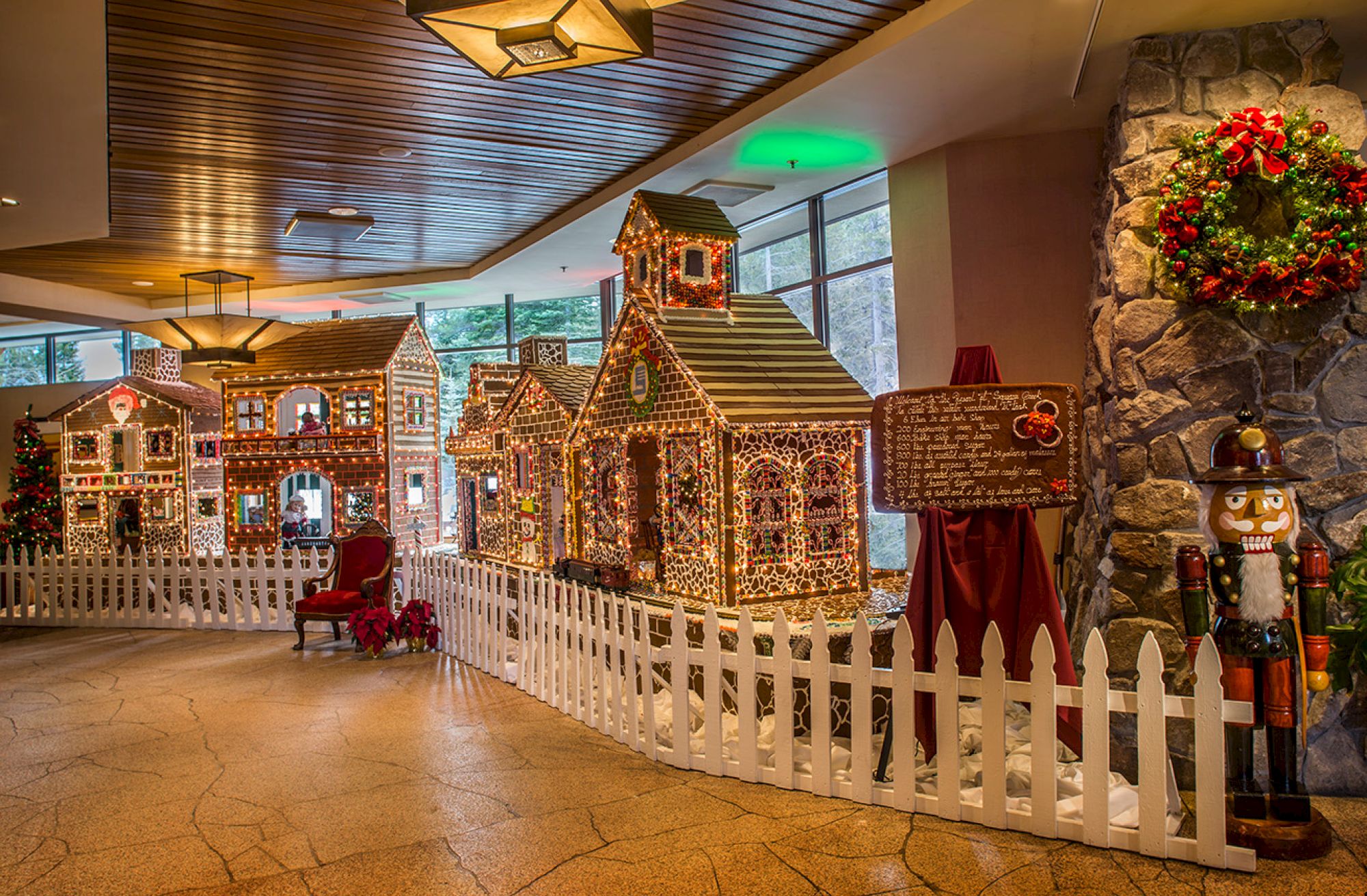 A festive indoor display featuring gingerbread houses, a white picket fence, a red chair, a nutcracker statue, and holiday decorations.